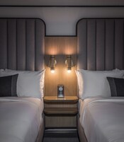 Un dormitorio con dos camas, una mesita de noche con un reloj e iluminación en la pared.