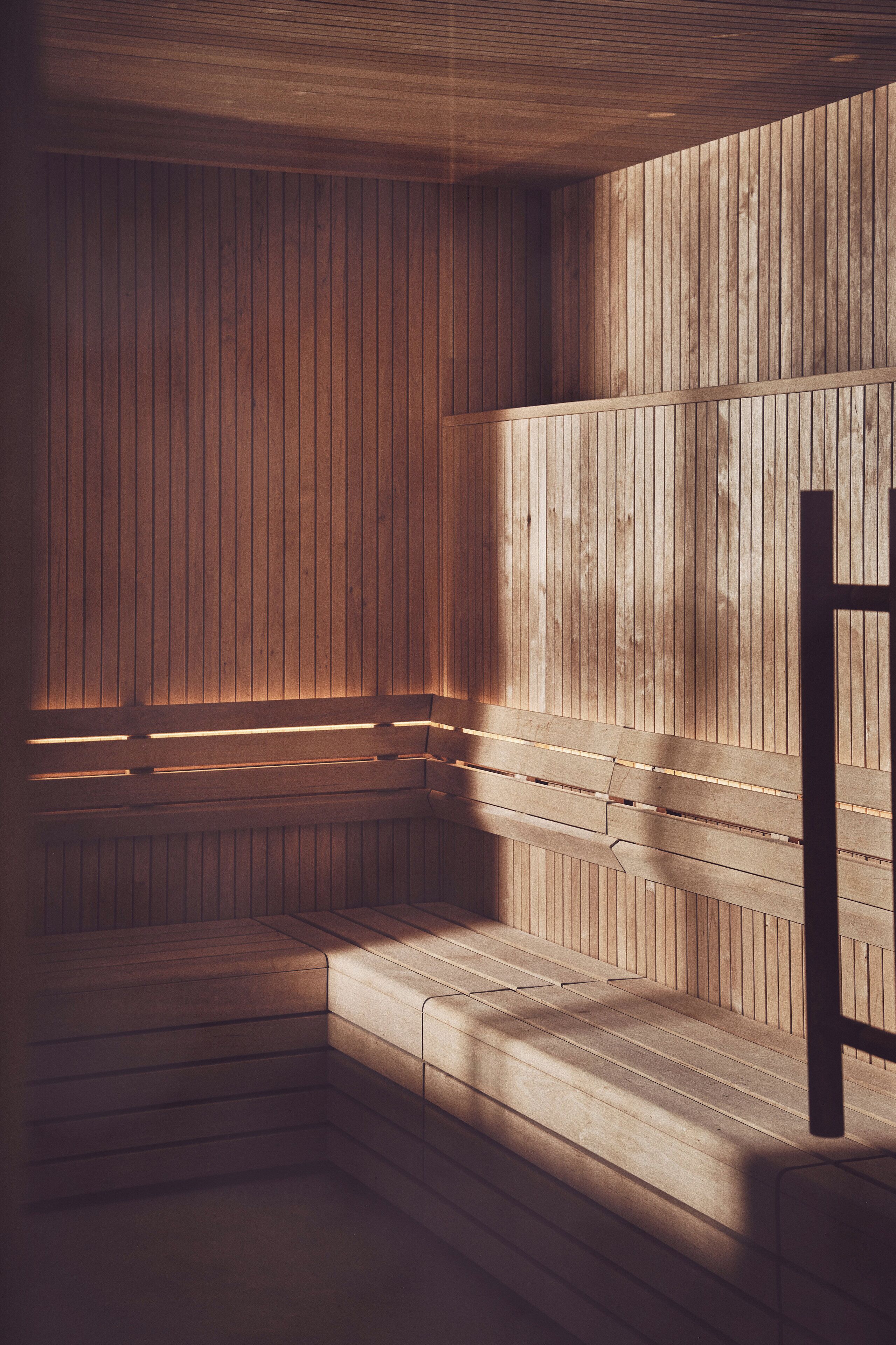 A sauna with wooden walls and benches, a sloped ceiling, and a bench with a backrest.