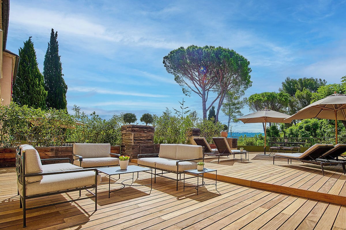 An outdoor patio with wooden flooring, lounge chairs, and umbrellas.