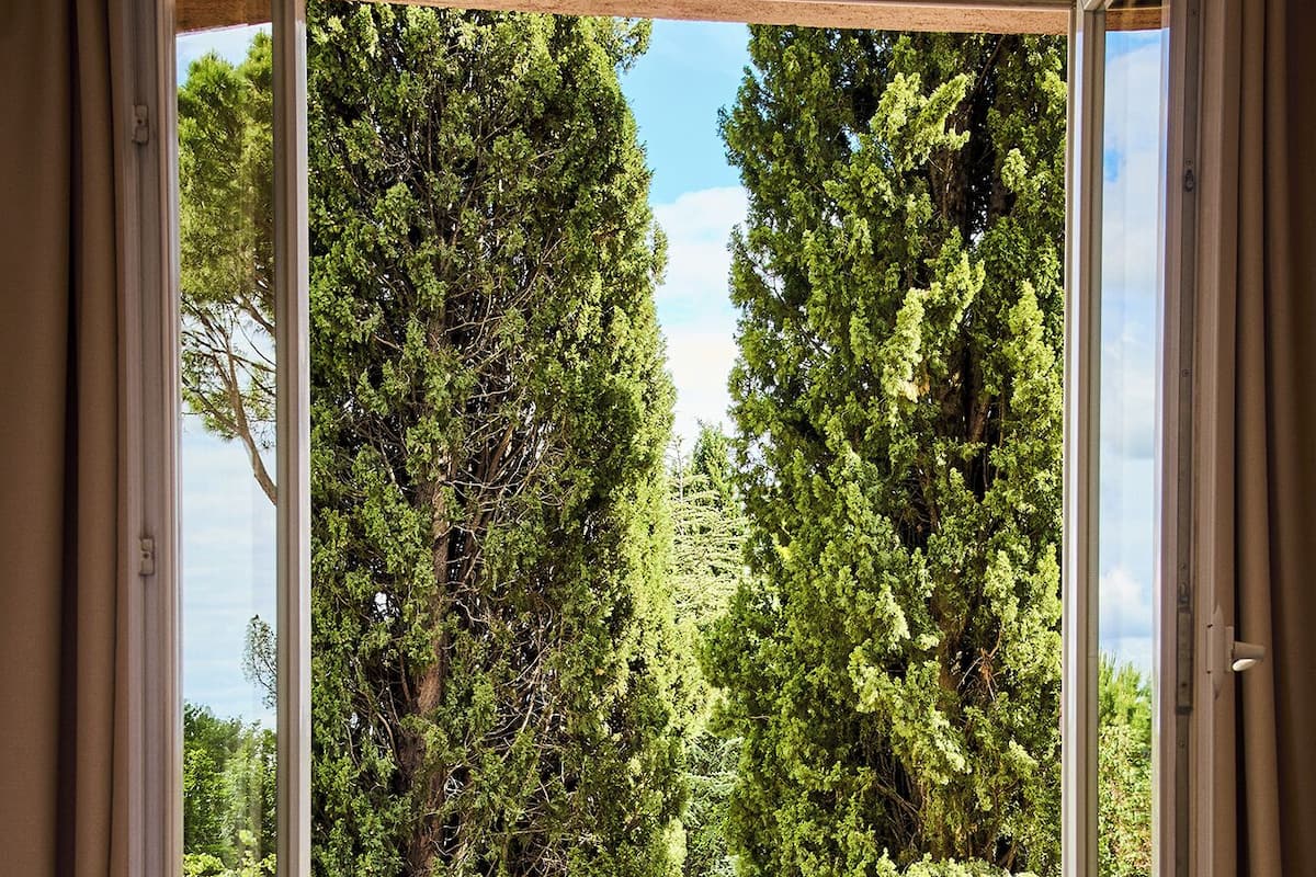 A bedroom with a large window overlooking a pool and lush greenery.