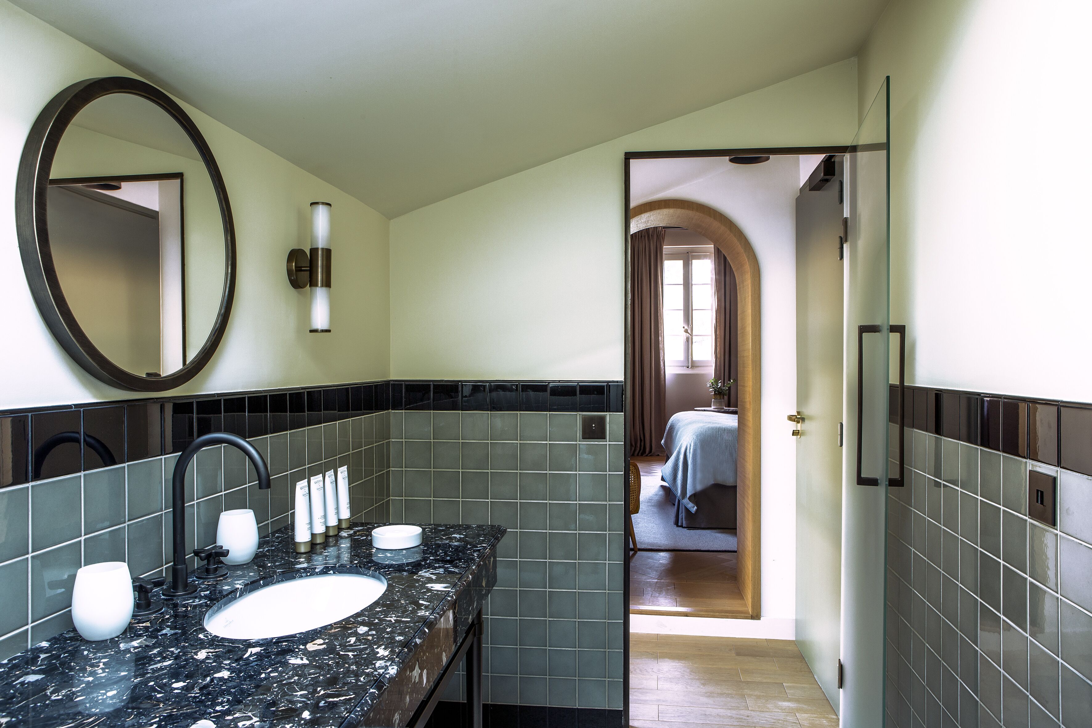 Une salle de bain avec un lavabo en marbre noir, un grand miroir et un mur recouvert de carreaux.