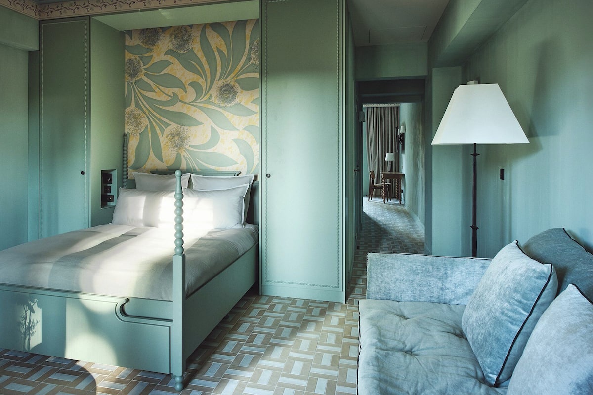A bedroom with a bed, a nightstand, a dresser, a lamp, and a patterned wall.