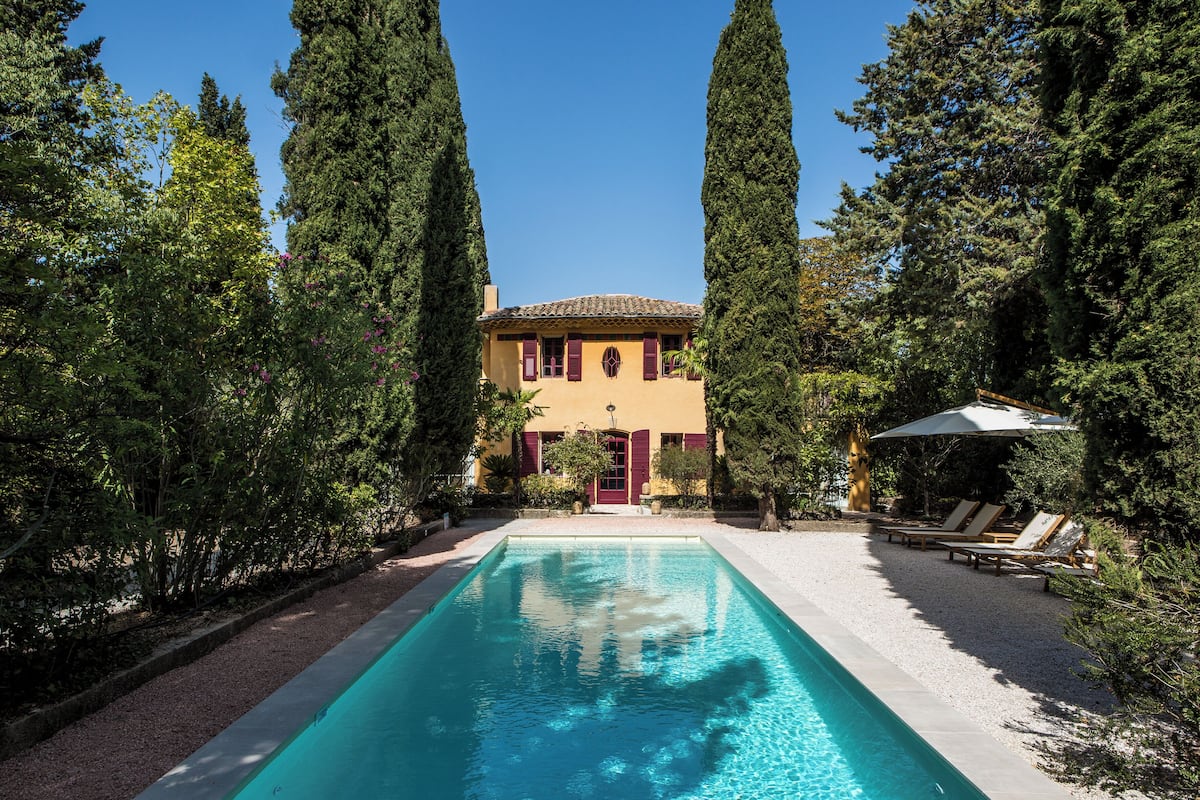 A swimming pool with a building in the background, surrounded by tall trees.
