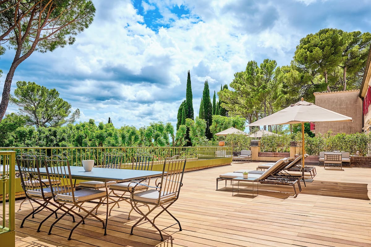 An outdoor patio with a wooden deck, metal chairs, a table, and lounge chairs.