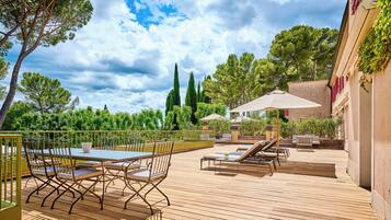 Un patio exterior con terraza de madera, sillas metálicas, una mesa y sillones de descanso.