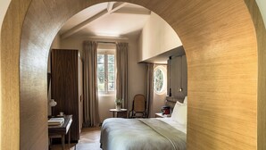 Un dormitorio con un arco de madera, una cama, un escritorio con lámpara, una silla y una ventana con cortinas.