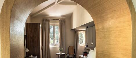Een slaapkamer met een houten boog, een bed, een bureau met lamp, een stoel en een raam met gordijnen.