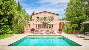 Una casa grande con piscina, rodeada de exuberante vegetación y un cielo azul despejado.