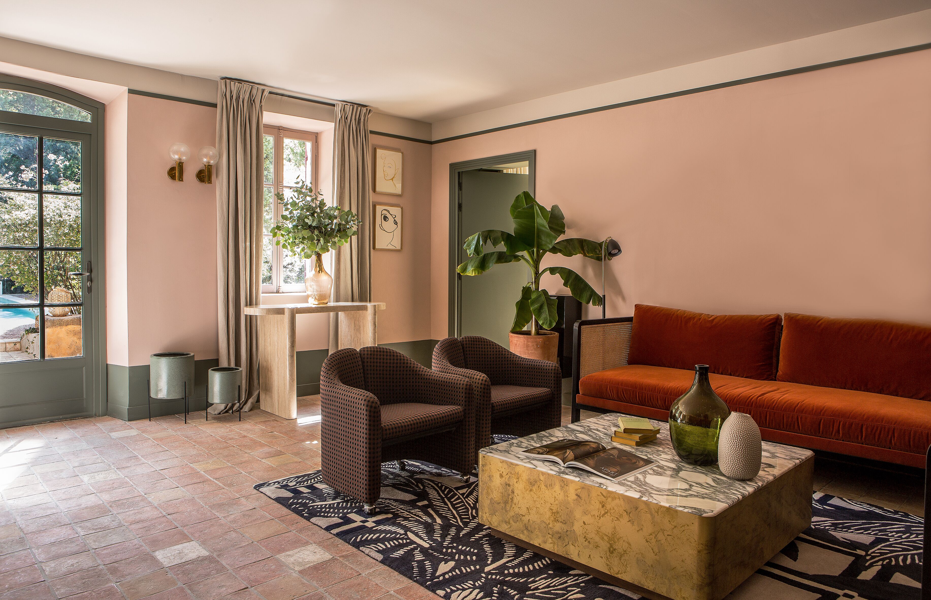 A living room with a sofa, two armchairs, a coffee table, a large plant, and a window with curtains.