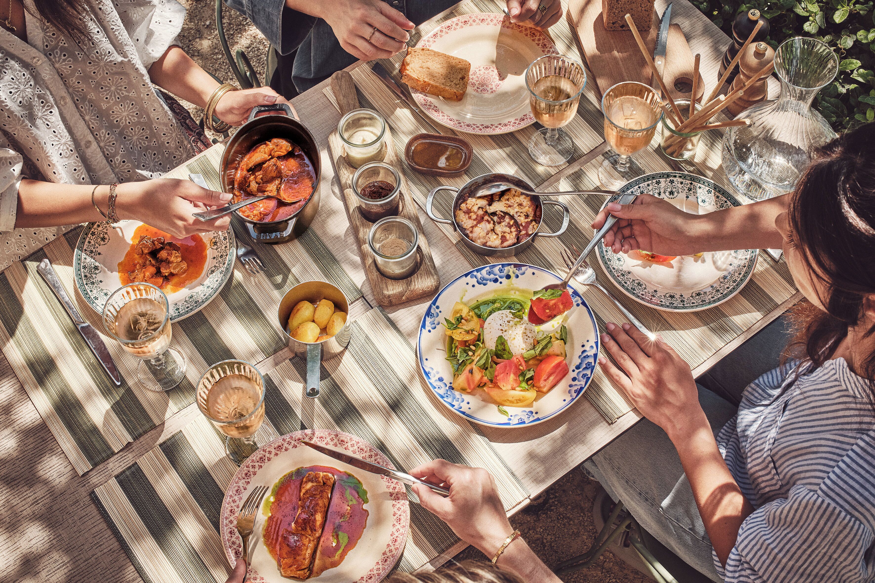 A group of people dining at an outdoor table with various dishes and drinks.