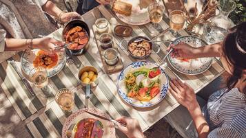 A group of people dining at an outdoor table with various dishes and drinks.