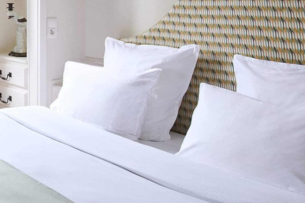 A neatly made bed with white linens and pillows, a patterned headboard, and a white nightstand with drawers.