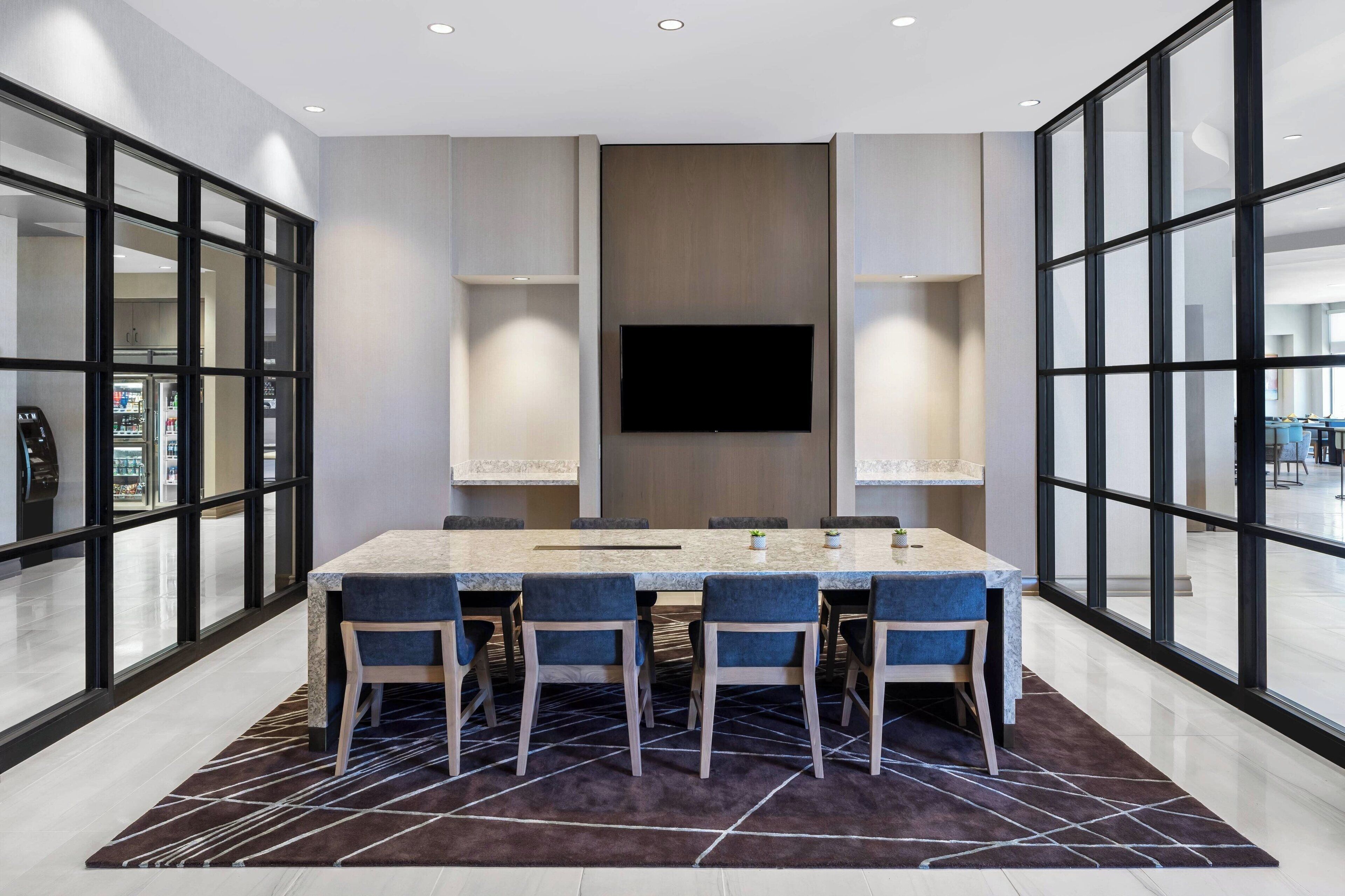 Un comedor moderno con una mesa grande, cuatro sillas, un televisor de pantalla plana y ventanas amplias.