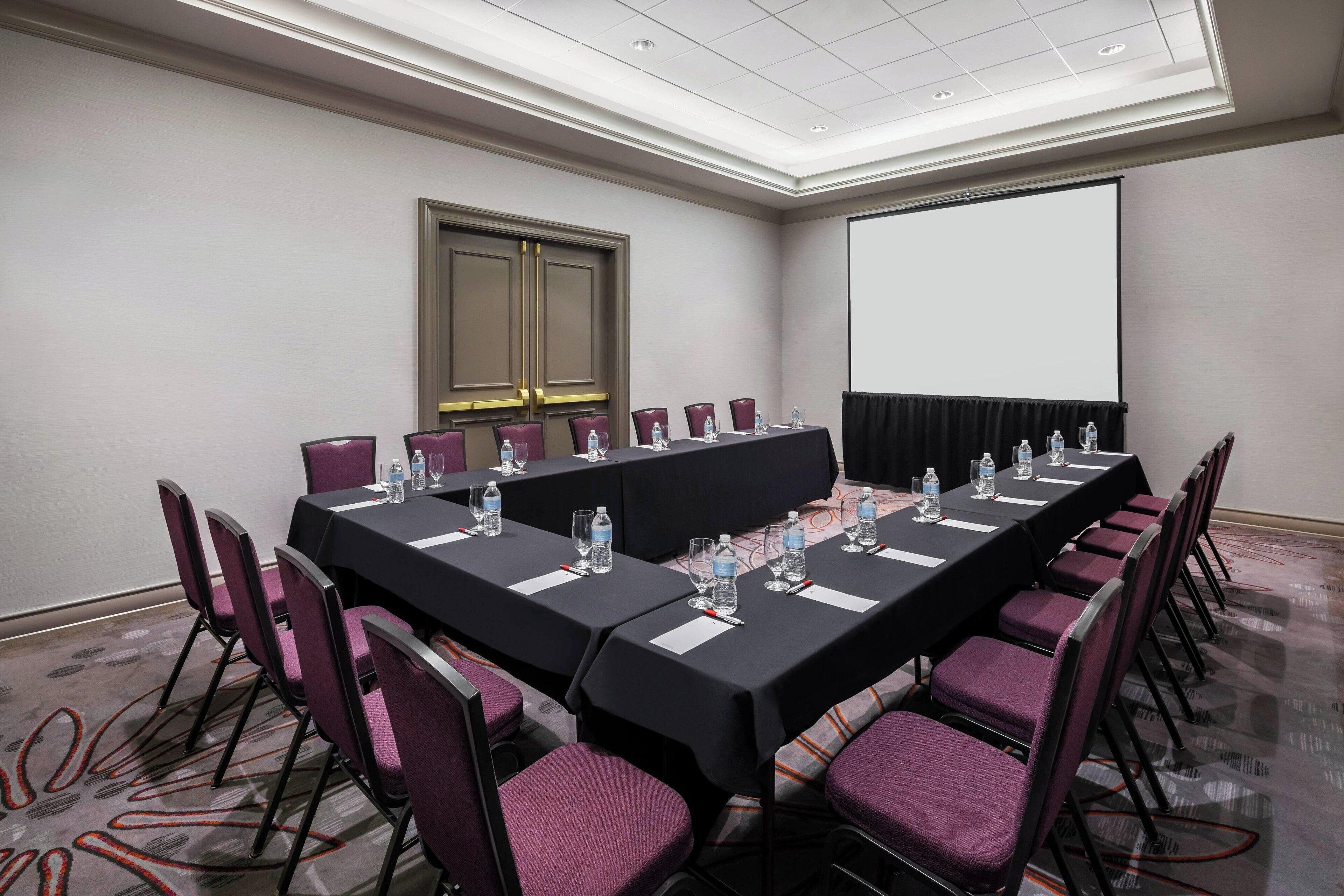 A conference room with a long table, chairs, a projector screen, and a door.