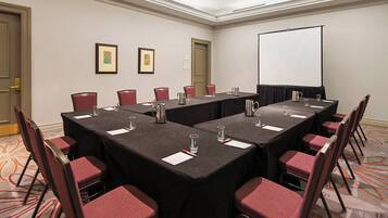Ein Konferenzraum mit einem langen Tisch, Stühlen, einer Projektionsleinwand und gerahmten Bildern an der Wand.