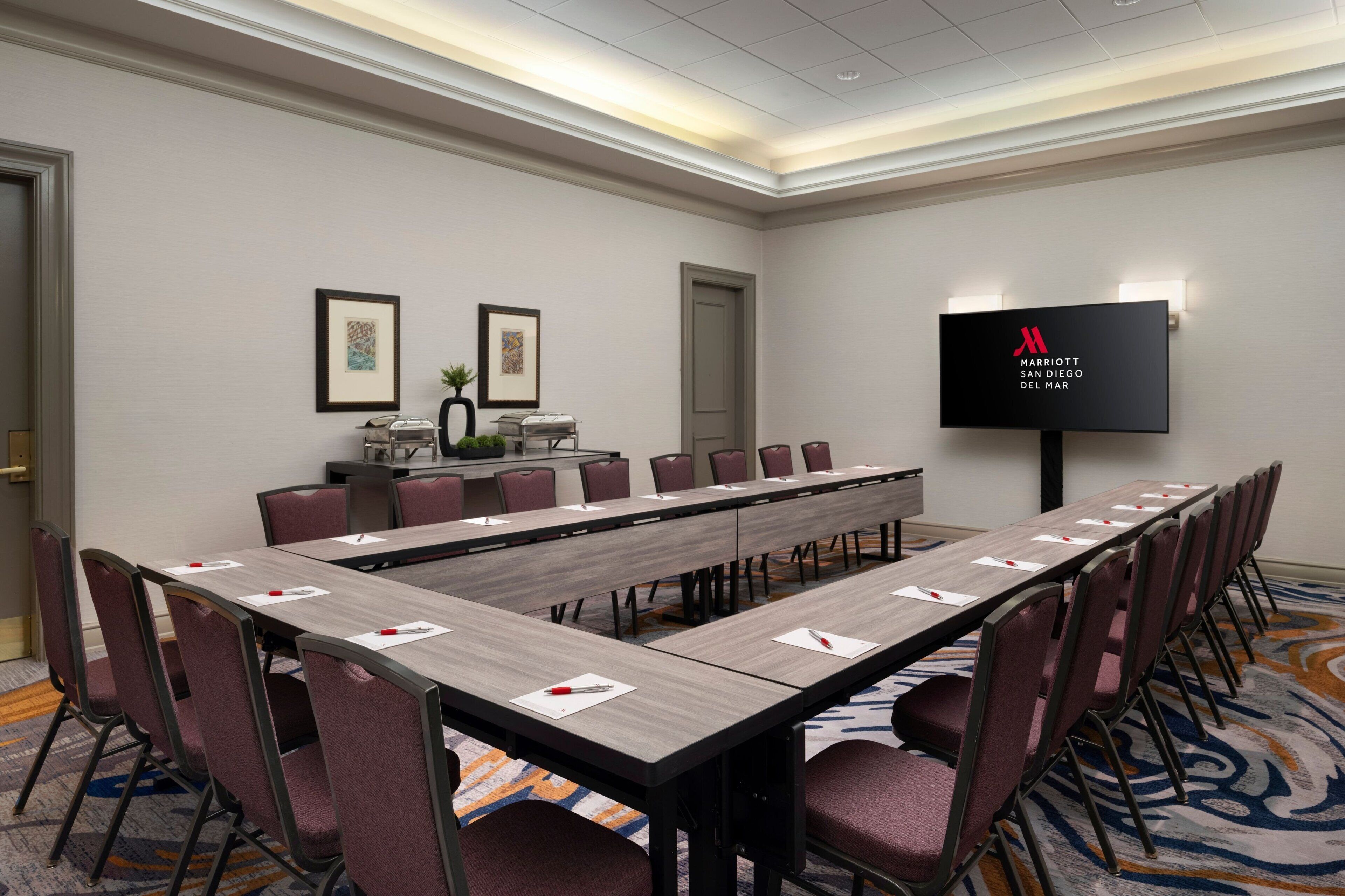A conference room with a long table, chairs, a TV screen, and framed artwork on the walls.