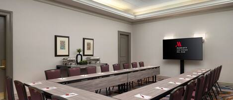 A conference room with a long table, chairs, a TV screen, and framed artwork on the walls.