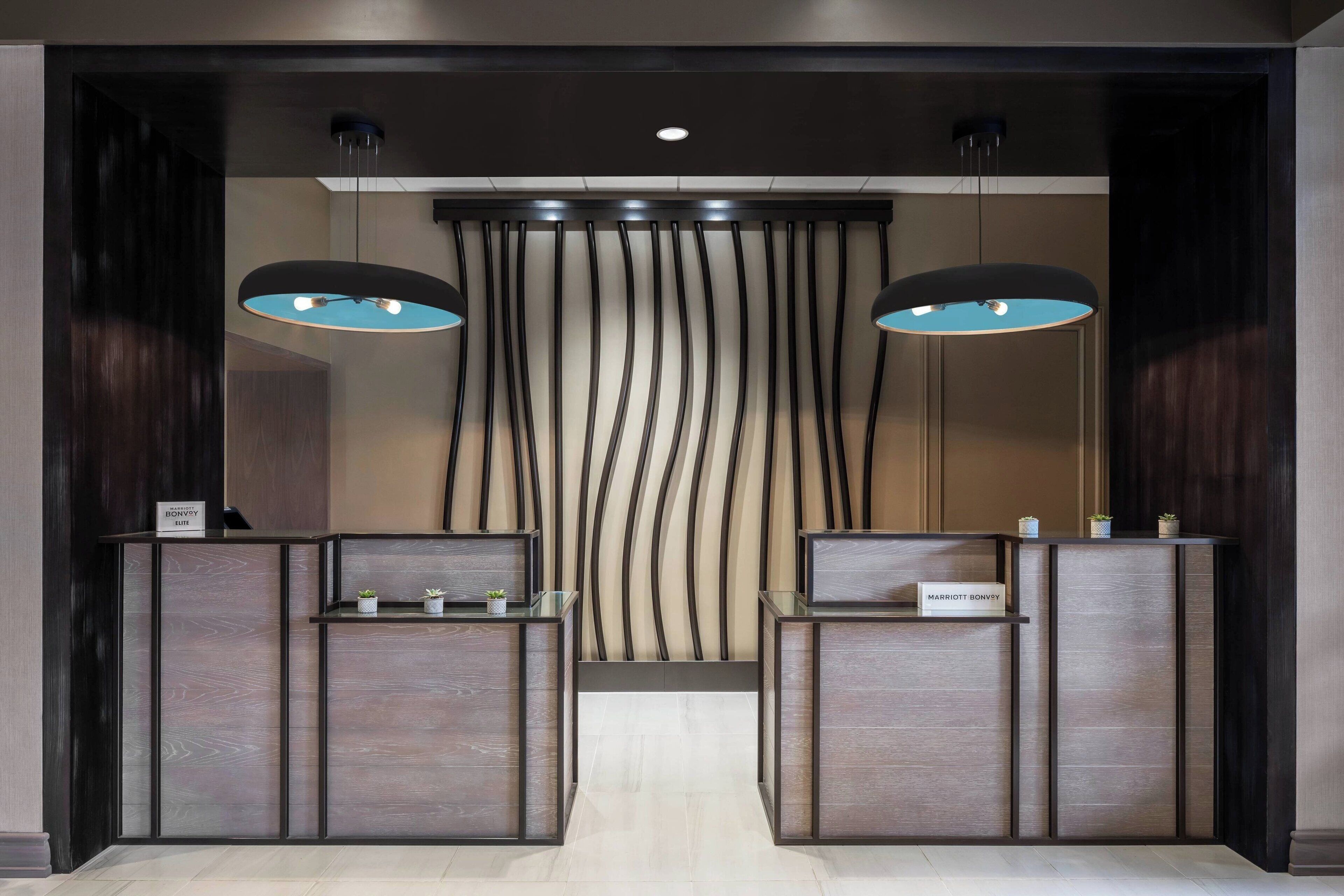 Un espace d’accueil doté de deux comptoirs de réception, d’un luminaire moderne et d’un panneau décoratif en bois vertical sur le mur.