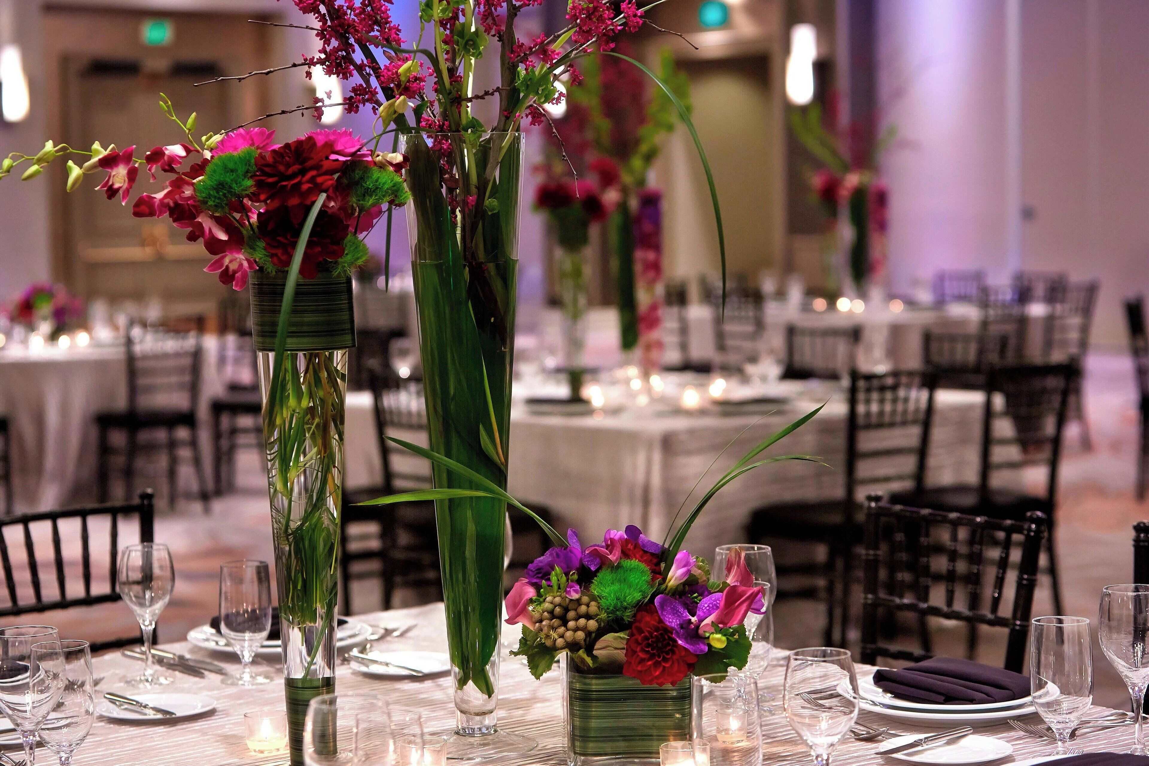 Un comedor con mesas dispuestas para el servicio, destacando altos jarrones con arreglos florales y velas.