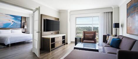 A modern hotel room with a bed, a TV, a sofa, and a balcony with a view.