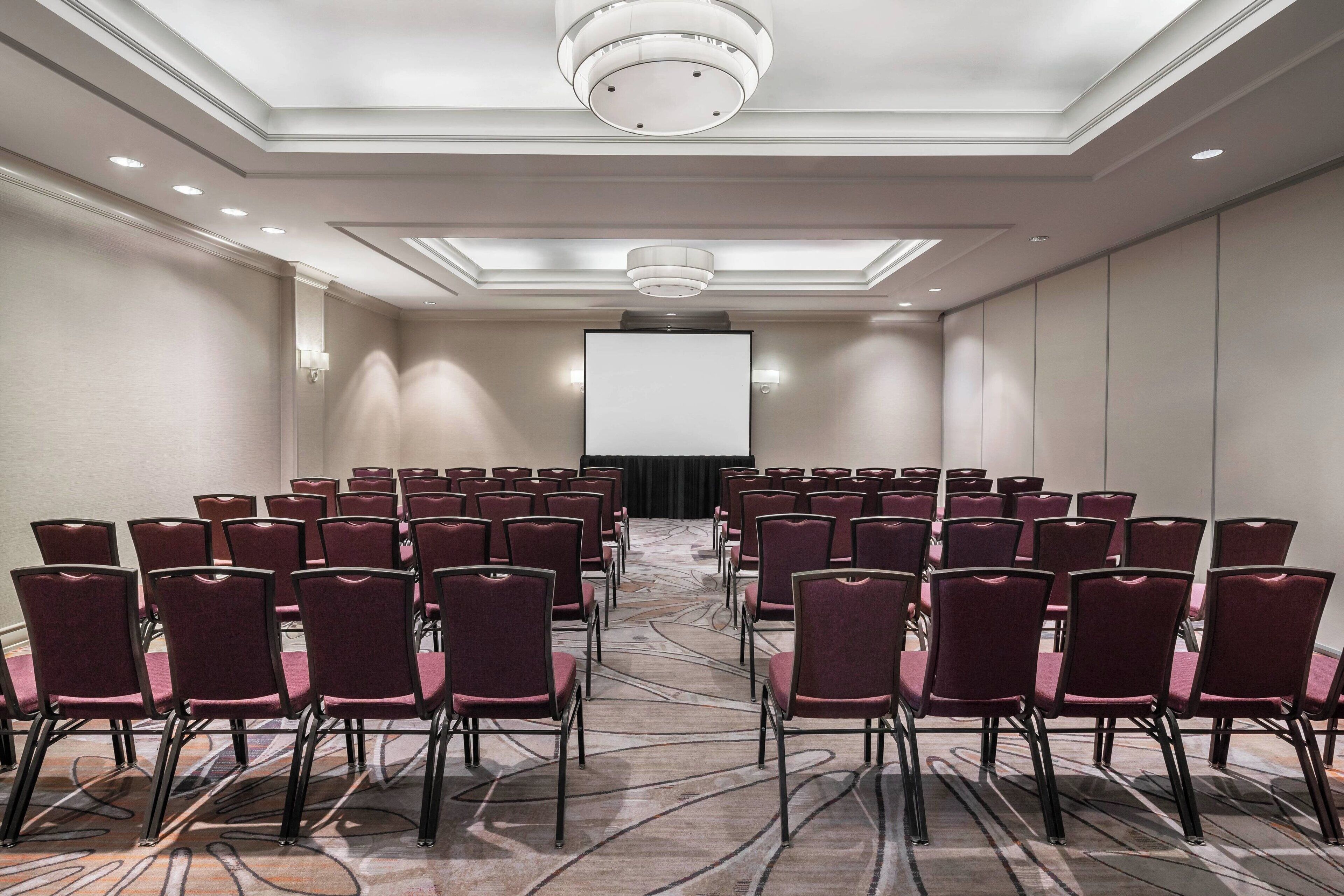 Un salón de conferencias con filas de sillas, una pantalla grande y un atril.