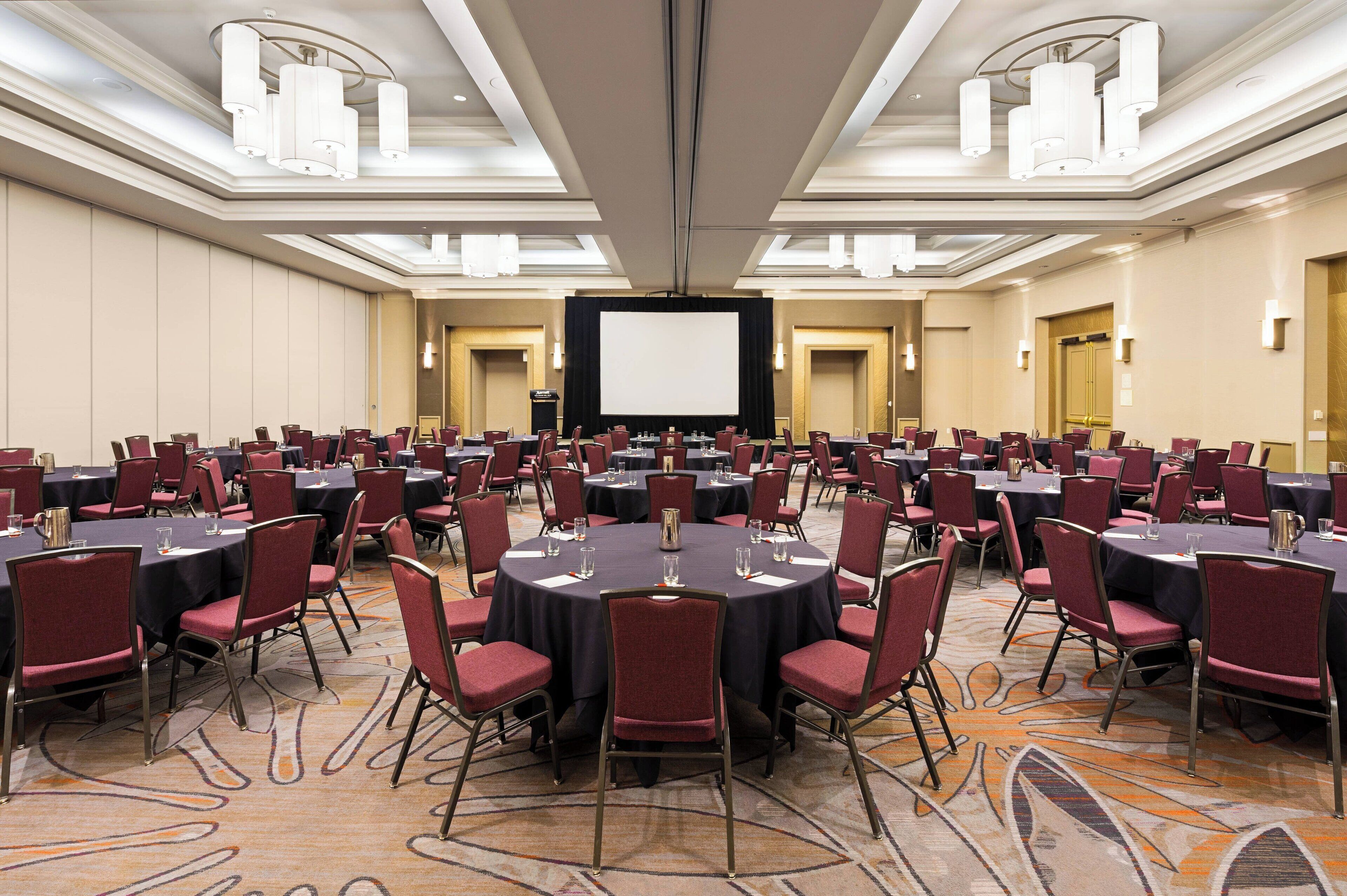 Une salle de conférence équipée de plusieurs tables rondes, de chaises rouges et d’un grand écran situé au fond de la pièce.
