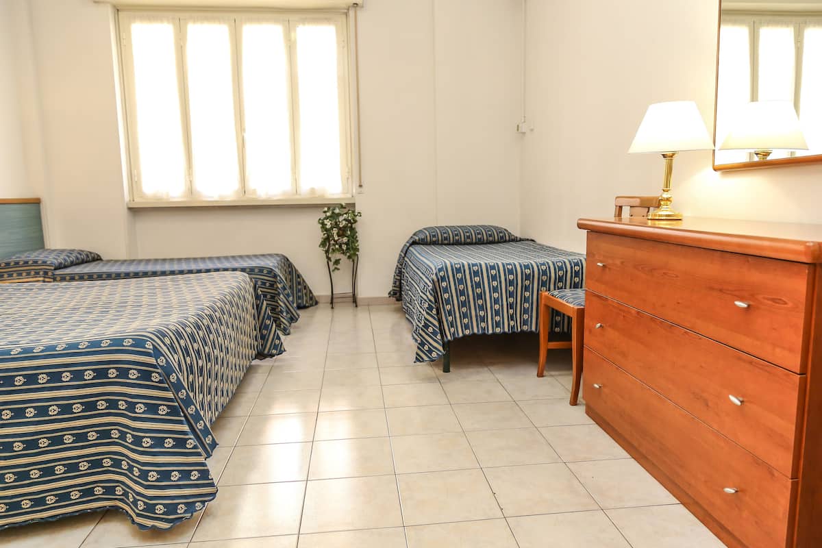 A bedroom with two beds, a dresser, a lamp, and a window.