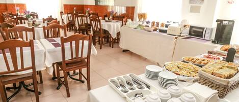 A dining area with multiple tables and chairs, a buffet with various food items, and a microwave on a counter.