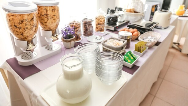 Una mesa de buffet con diversos alimentos y recipientes, incluyendo cereales, leche y salsas.