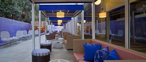 Ein Außenbereich mit Loungemöbeln aus Rattan, einem runden Couchtisch und einem roten Sofa mit blauen Kissen.