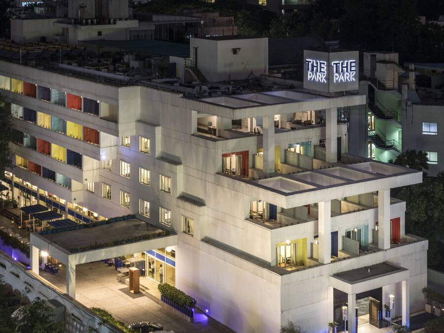A multi-story hotel with a rooftop terrace, a sign reading "The Park," and a parking area with cars.