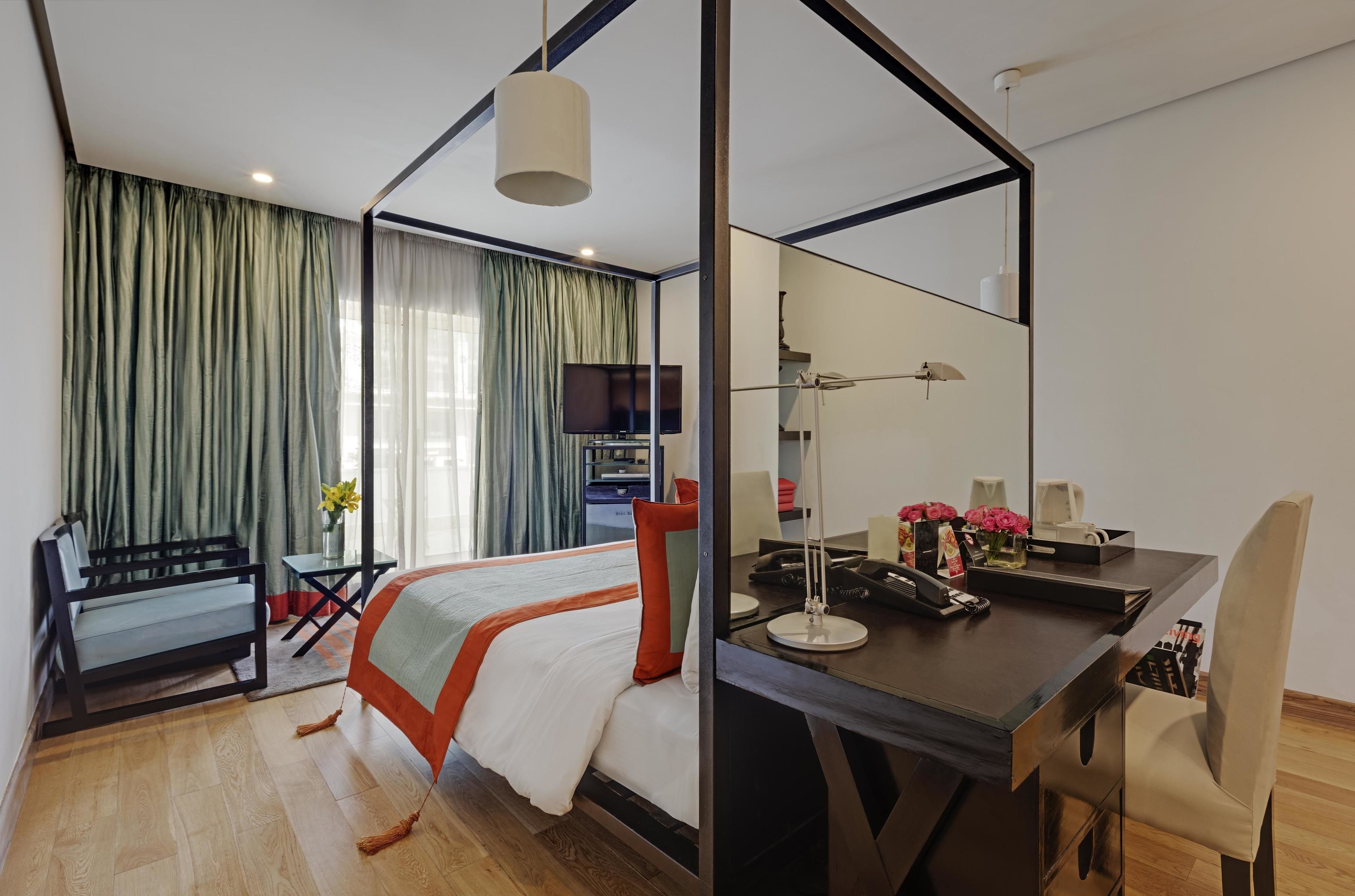 A modern hotel room with a bed, desk, chair, and a large mirror.