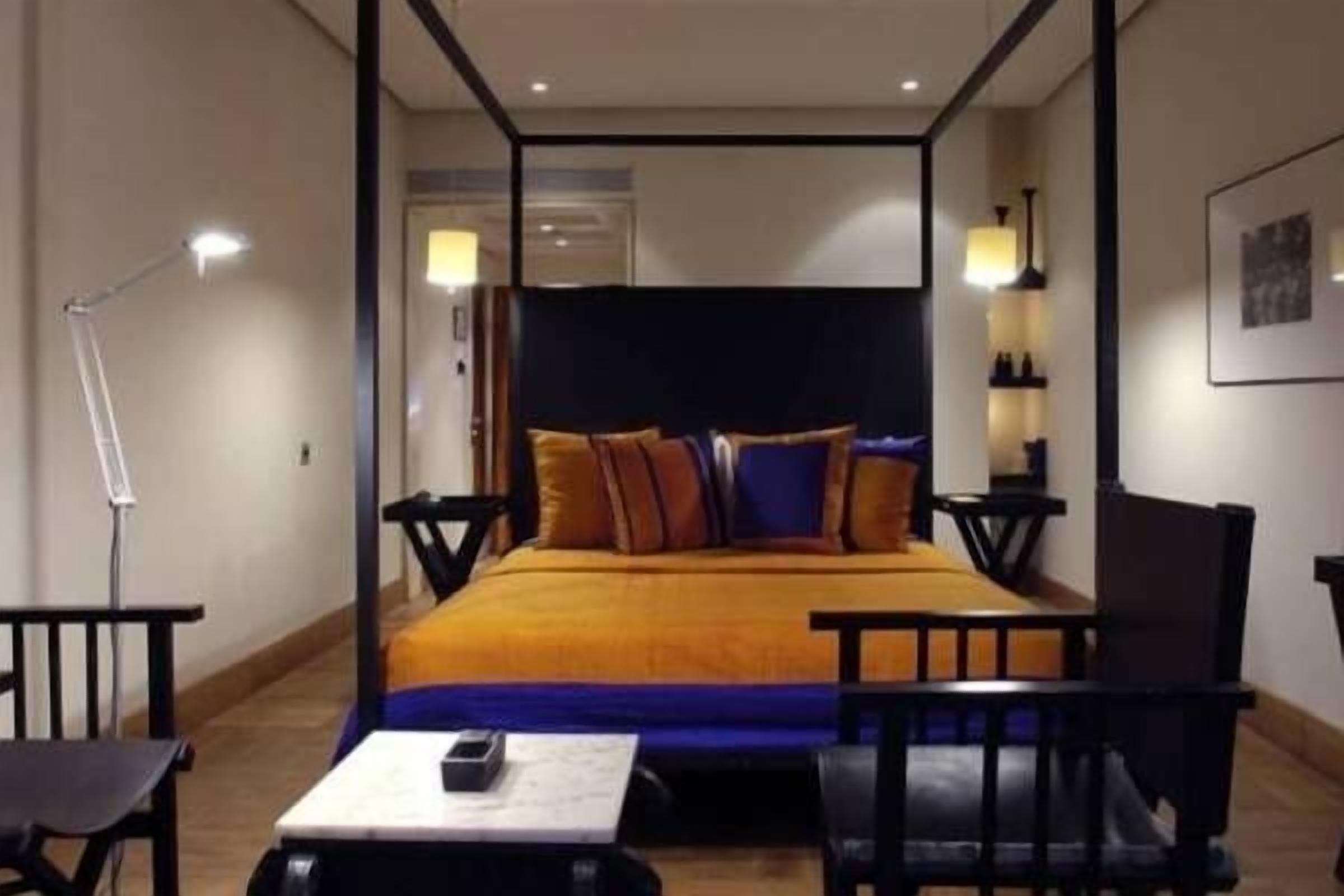A hotel room with a four-poster bed, a desk with a chair, and a bedside table.