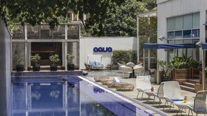 Un espace piscine avec des chaises longues et des tables, un panneau indiquant « AQUA », et un bâtiment moderne doté de grandes fenêtres.
