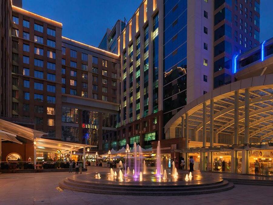 A modern hotel with a central fountain, multiple floors, and a covered walkway.