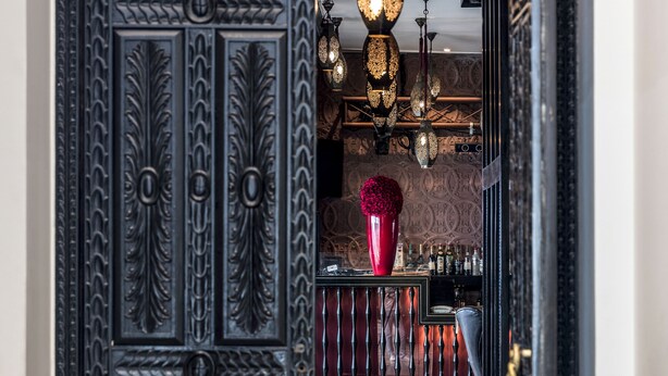 Un espace bar agrémenté de portes en métal noir ouvragé, d’un vase rouge et de luminaires en laiton suspendus.