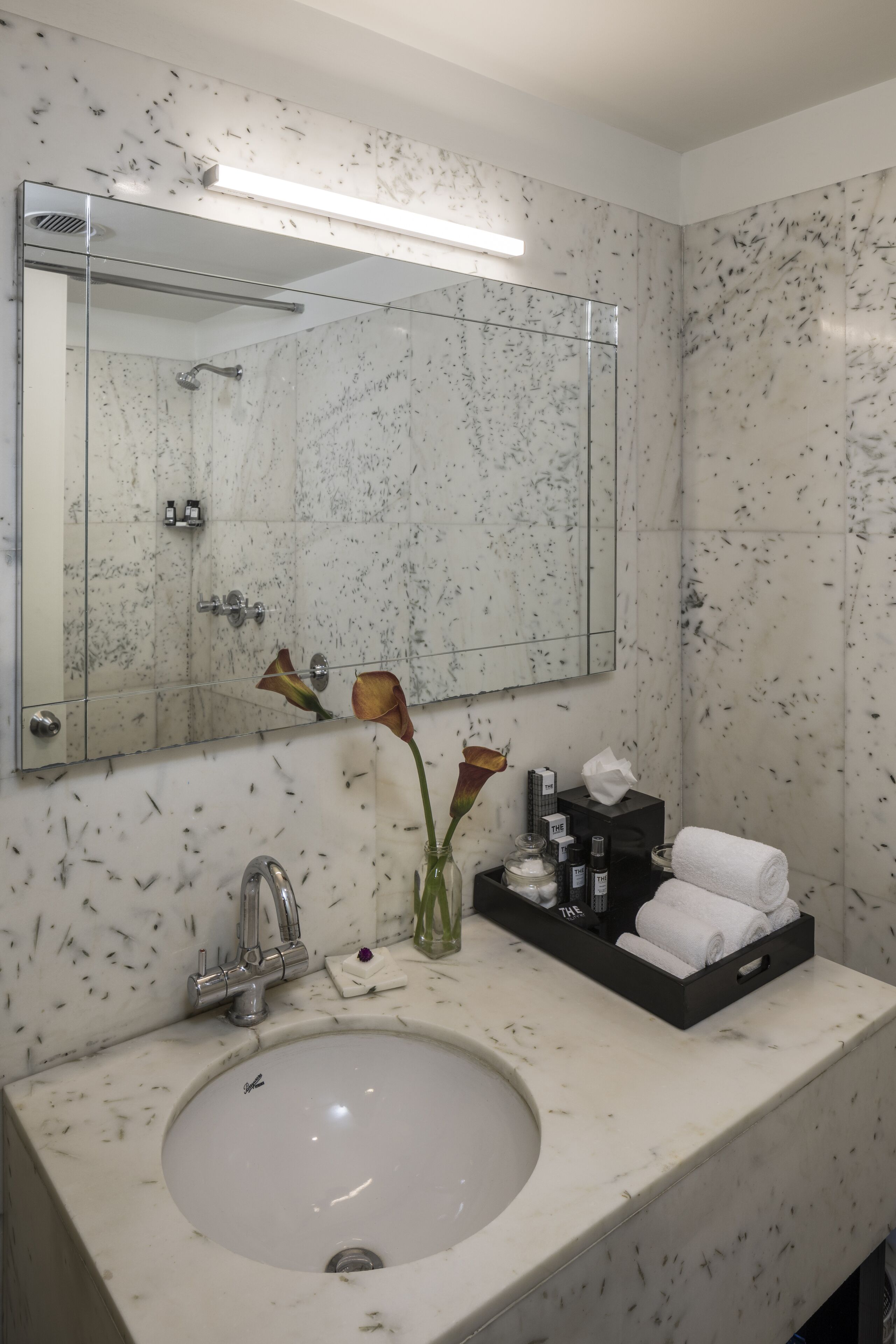 A bathroom with a marble sink, a mirror, a towel rack, and toiletries.
