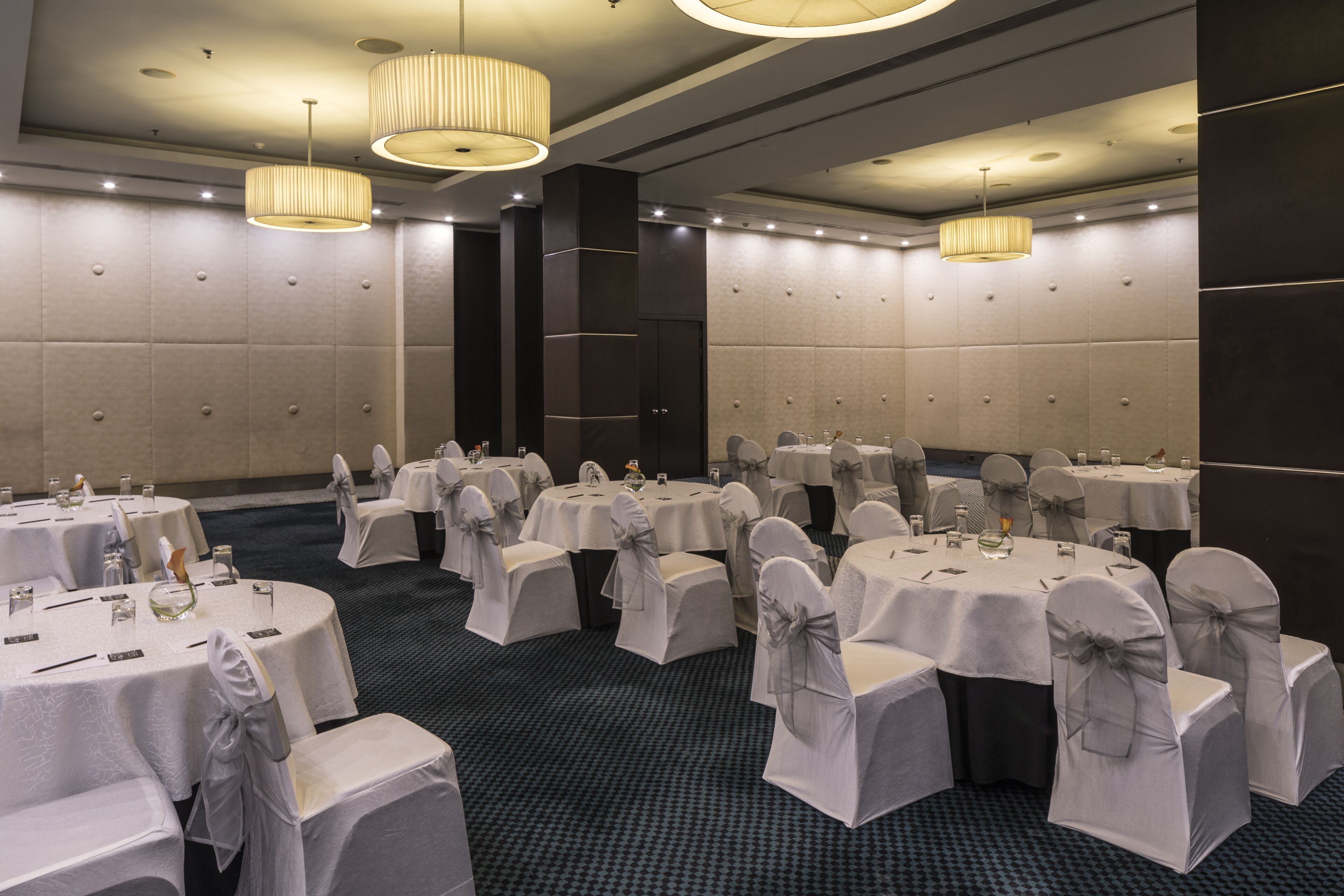 A banquet hall with round tables, each with a white tablecloth and chairs with gray sashes.