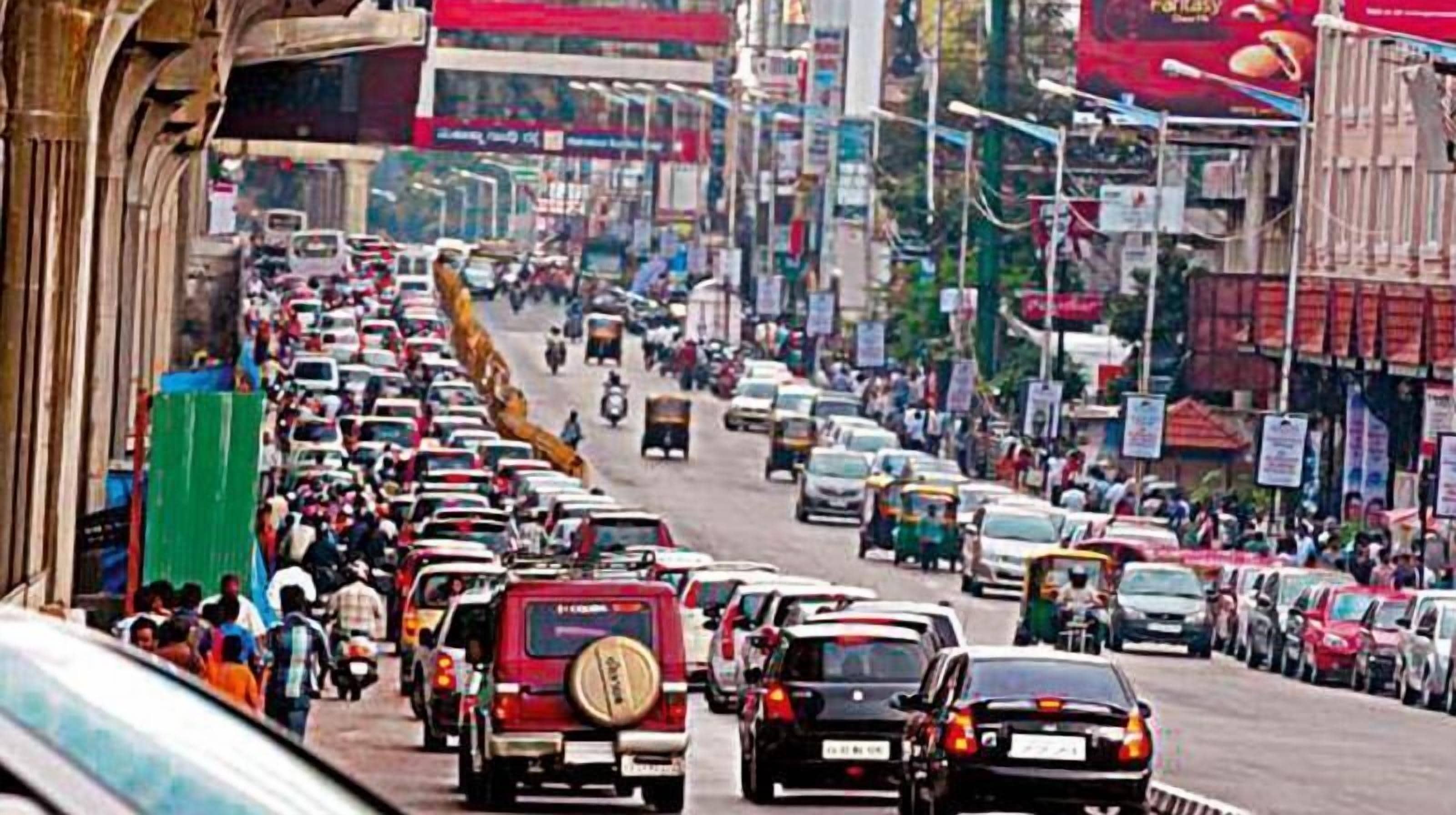 A busy urban street with multiple lanes of traffic, including cars, motorcycles, and auto-rickshaws.