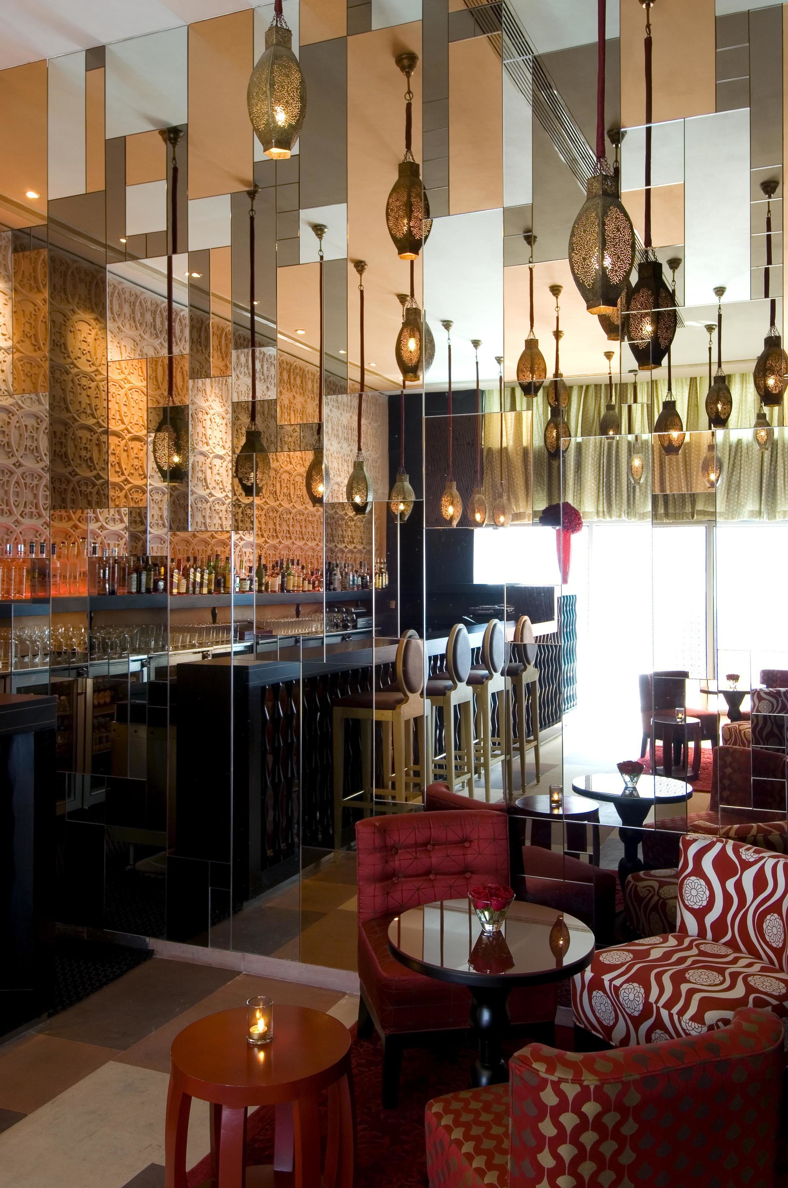 A bar area with a mirrored wall, hanging lanterns, and seating arrangements.