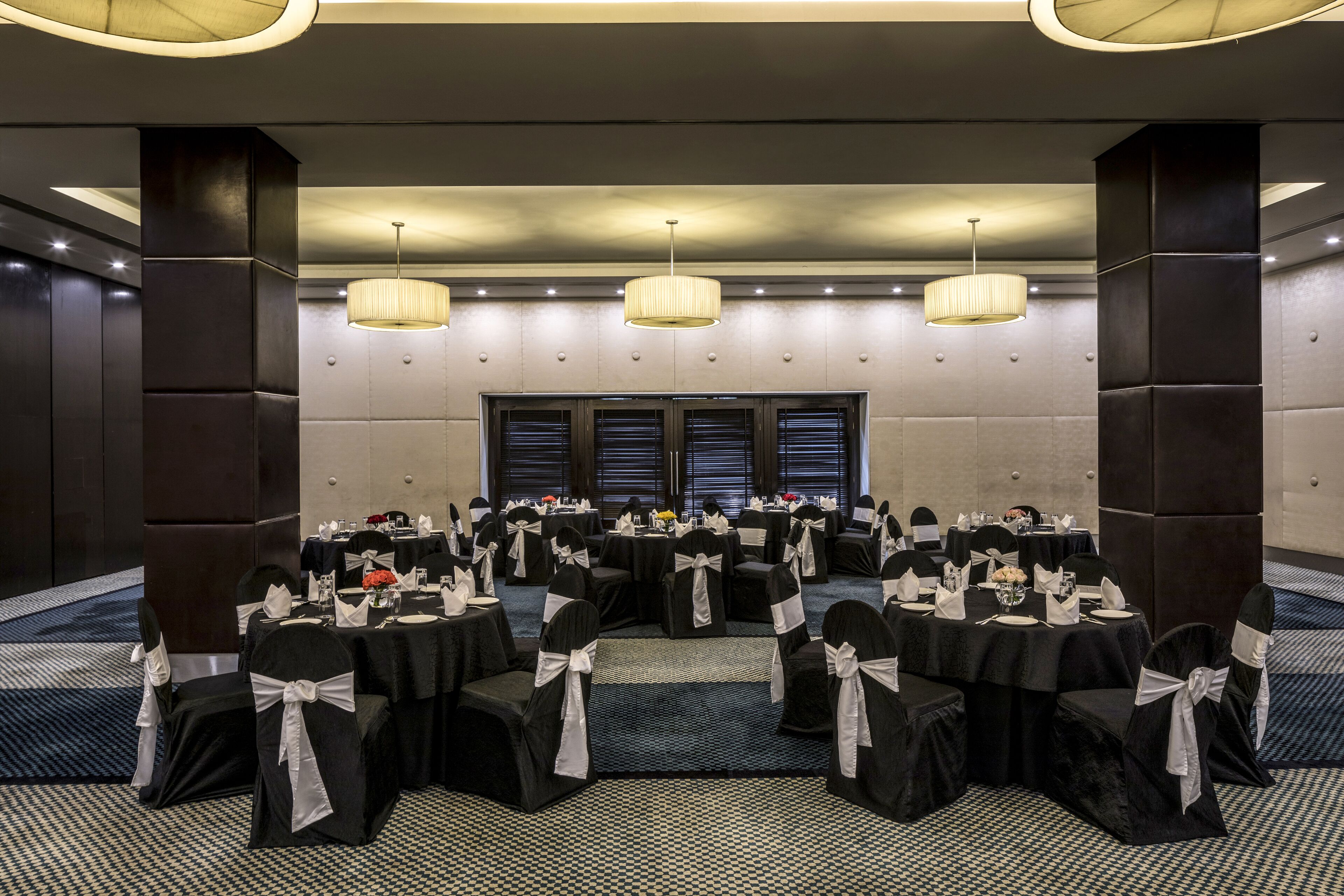 Un salón de conferencias con mesas redondas, sillas negras con cintas blancas y candelabros.