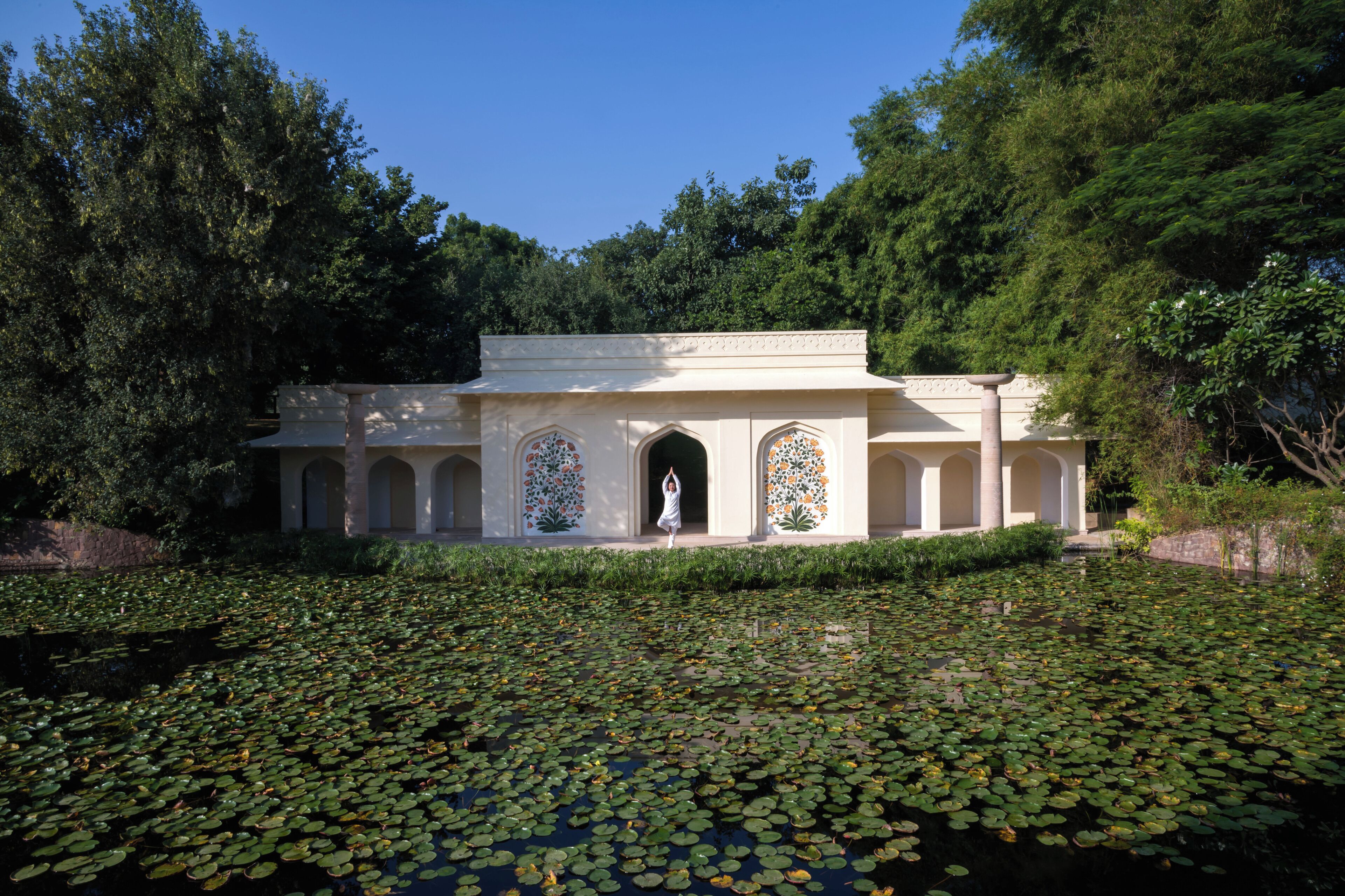 A building with a central arched doorway, surrounded by a water body with lily pads.