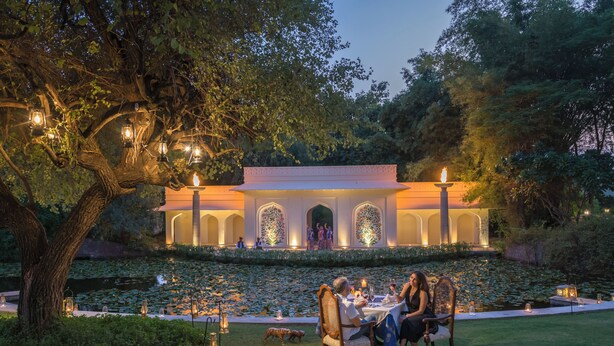 An outdoor dining area with a table set for two, surrounded by lush greenery and a pond. - The Oberoi Vanyavilas, Ranthambore (Sawai Madhopur)