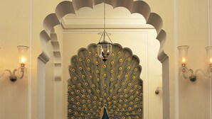 A dining area with a peacock-themed wall, a chandelier, and two chairs. - The Oberoi Vanyavilas, Ranthambore (Sawai Madhopur)