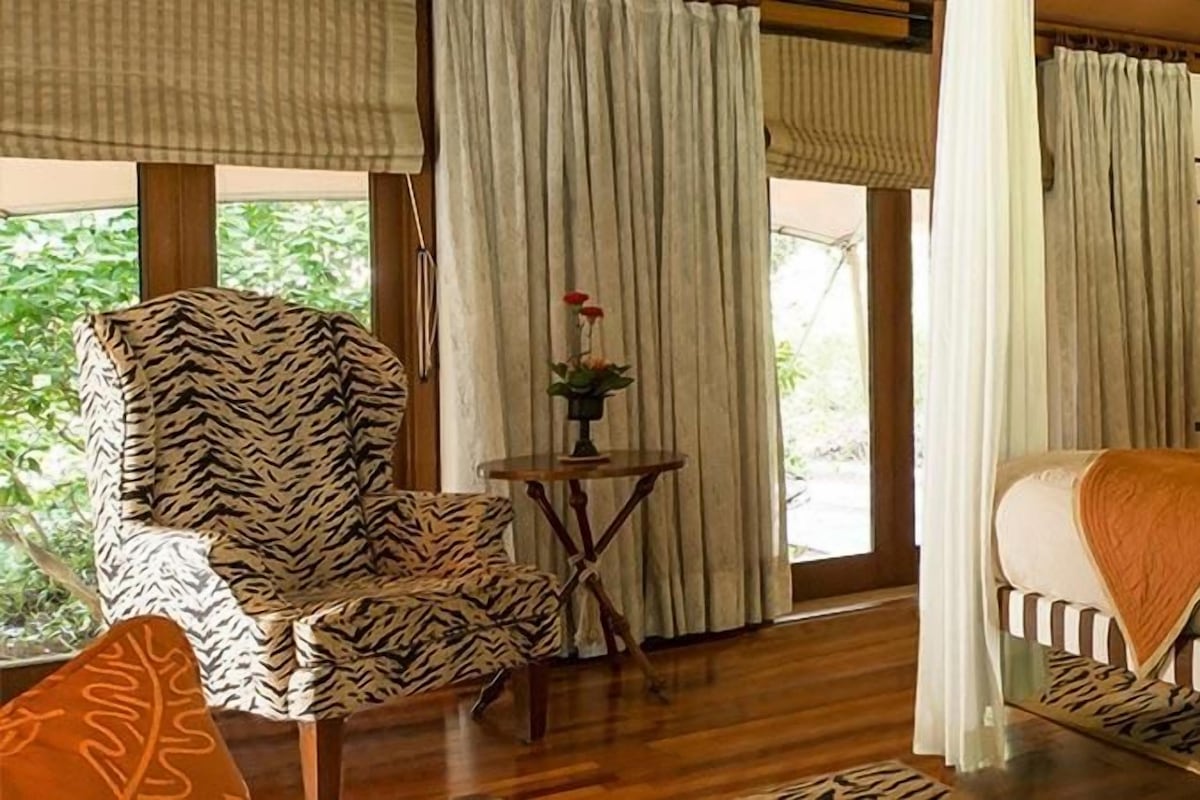 Una habitación con cama, una silla, una mesita y cortinas.