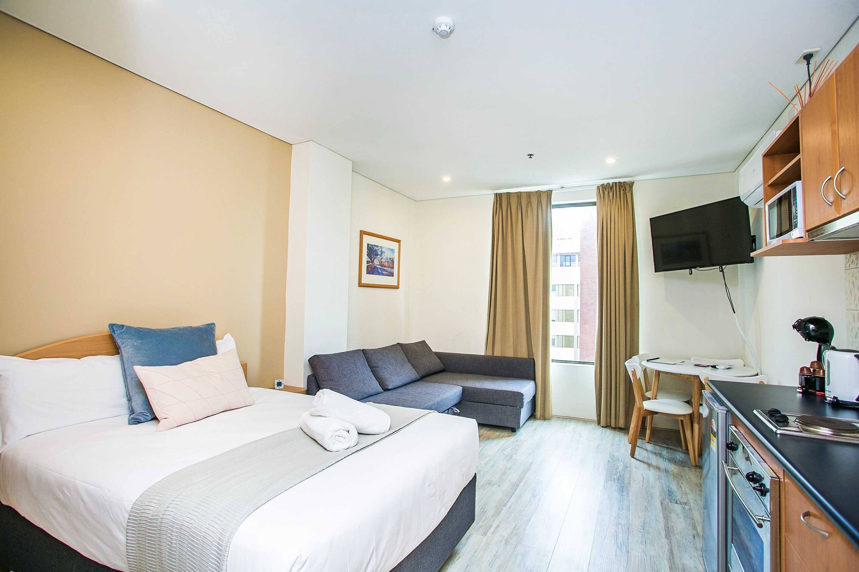 A hotel room with a bed, a sofa, a desk with a chair, a TV, and a microwave.