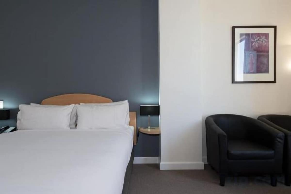 A hotel room with a bed, bedside tables, a chair, and a framed picture on the wall.