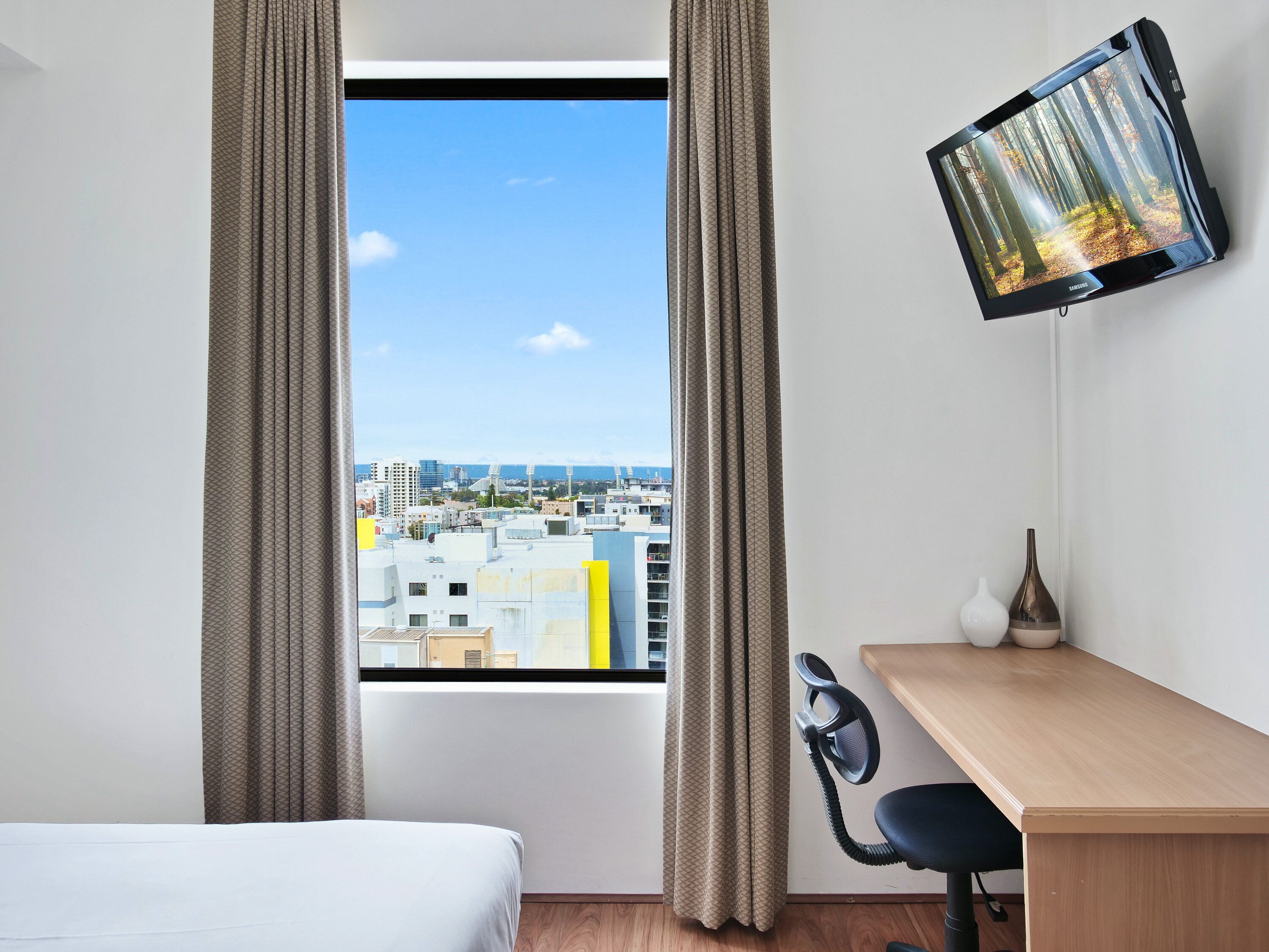 Ein Hotelzimmer mit Bett, Schreibtisch, Stuhl, Fernseher und einem Fenster mit Vorhängen.