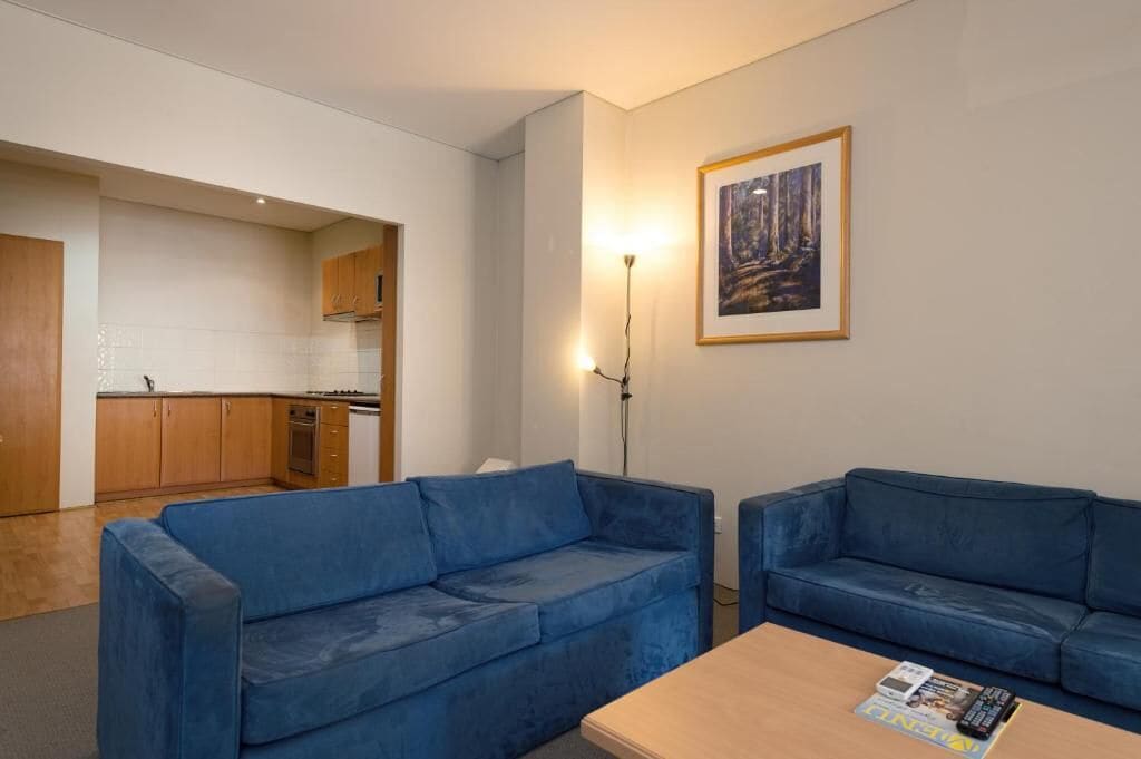 A modern living room with two blue sofas, a coffee table, and a framed painting on the wall.