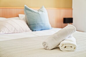 A neatly made bed with a rolled white towel, a blue pillow, and a white pillow.